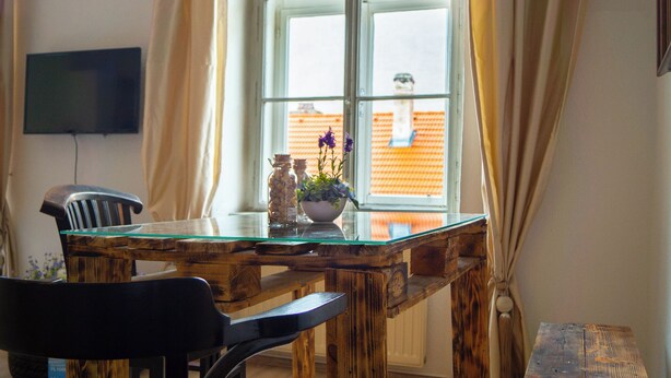 A wooden dining table with a glass top, a chair, and a vase with flowers. - Cozy 1BR Suited for Extended Comfort (Vienna)