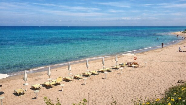 A beach with rows of sun loungers and umbrellas, a lifebuoy, and a clear view of the ocean. - Hotiday Castelsardo Spiaggia (Lu Bagnu)
