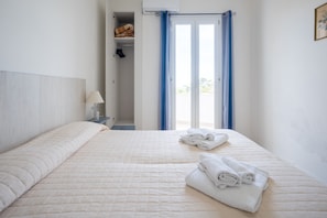 Ein Hotelzimmer mit Bett, Nachttisch, Lampe, Kleiderschrank und Blick durch eine Tür.