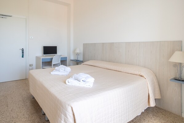 Una habitació d'hotel amb un llit, un escriptori amb un ordinador, una cadira i dues làmpades laterals.