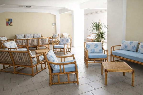 A spacious lounge area with wicker furniture and blue cushions, featuring a large potted plant and a view of the outdoors. - Hotiday Castelsardo Spiaggia (Lu Bagnu)