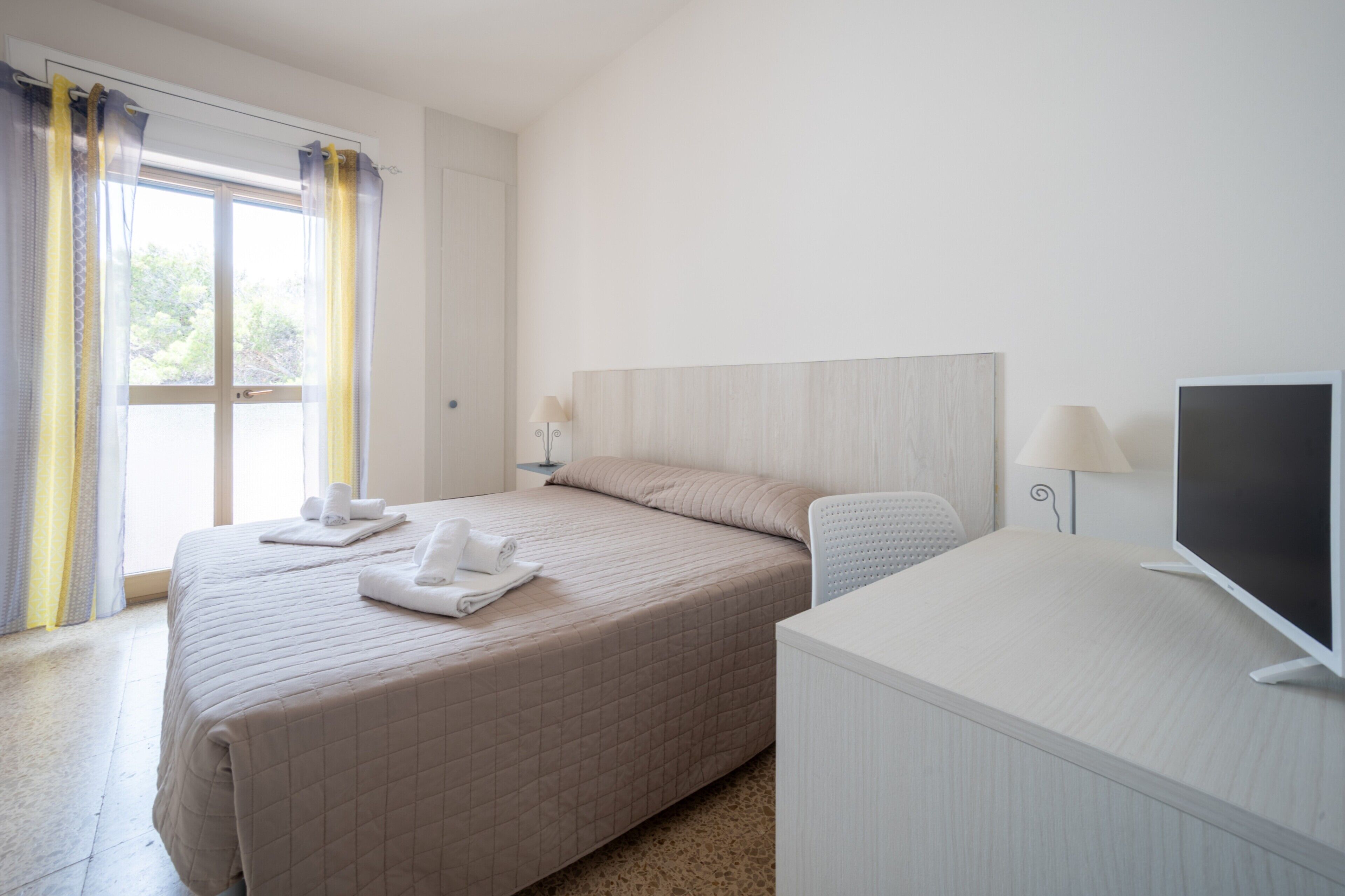 Een hotelkamer met een bed, een bureau, een televisie en een raam met gordijnen.