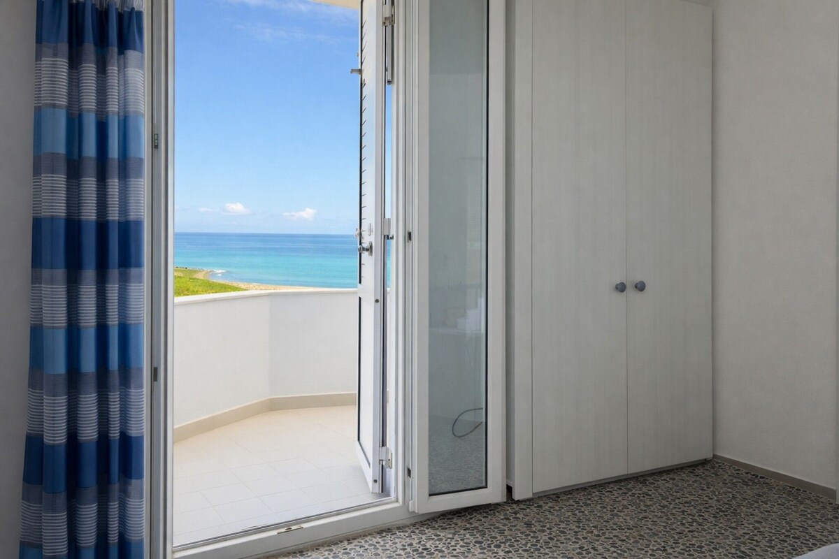 A room with a view of the ocean, a sliding glass door, and a tiled floor.