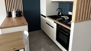 A modern kitchen with a wooden table, white chairs, a black stove, and a white cabinet. - Sea view apartment (Palavas-les-Flots)