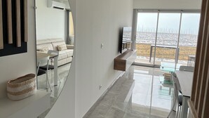 A modern interior with a large mirror, a sofa, and a dining area with a view of a cityscape. - Sea view apartment (Palavas-les-Flots)