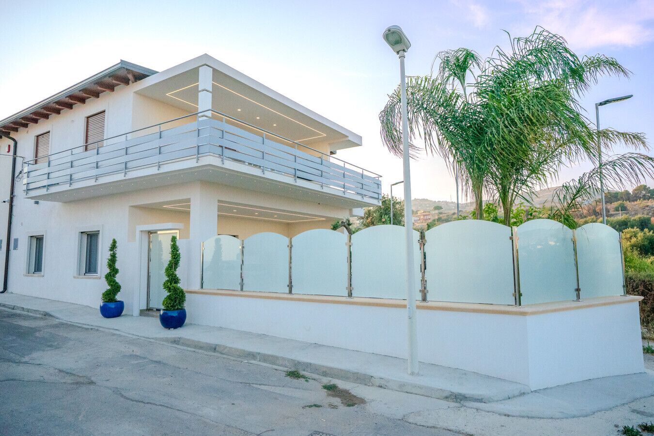 A modern two-story house with a balcony, a covered entrance, and a white fence with semi-transparent panels.