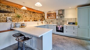 Une cuisine moderne dotée d’un grand îlot central, de meubles blancs et d’un mur d’accent en pierre.