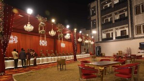 A banquet hall with a long table set for a formal event, surrounded by red chairs and chandeliers. - Hotel Awadh Grand (Kanpur)