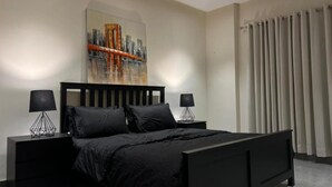 Quarto moderno com cama preta, duas mesas de cabeceira e uma pintura da paisagem urbana na parede.