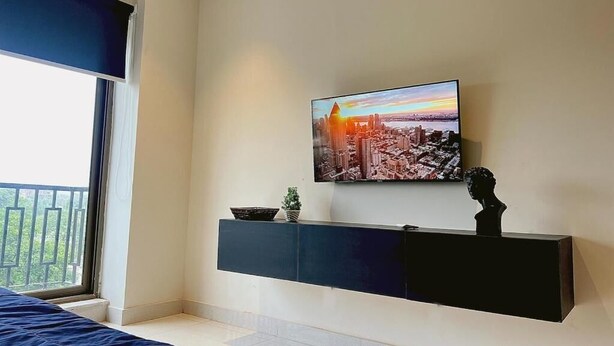 Quarto moderno com pintura de paisagem urbana, mesa de console preta e cama com cabeceira azul.