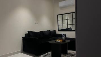 A modern living room with a black sofa, a round coffee table, and a large mirror on the wall.