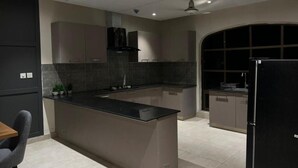 Uma cozinha moderna com ilha central, armários escuros e uma geladeira preta.