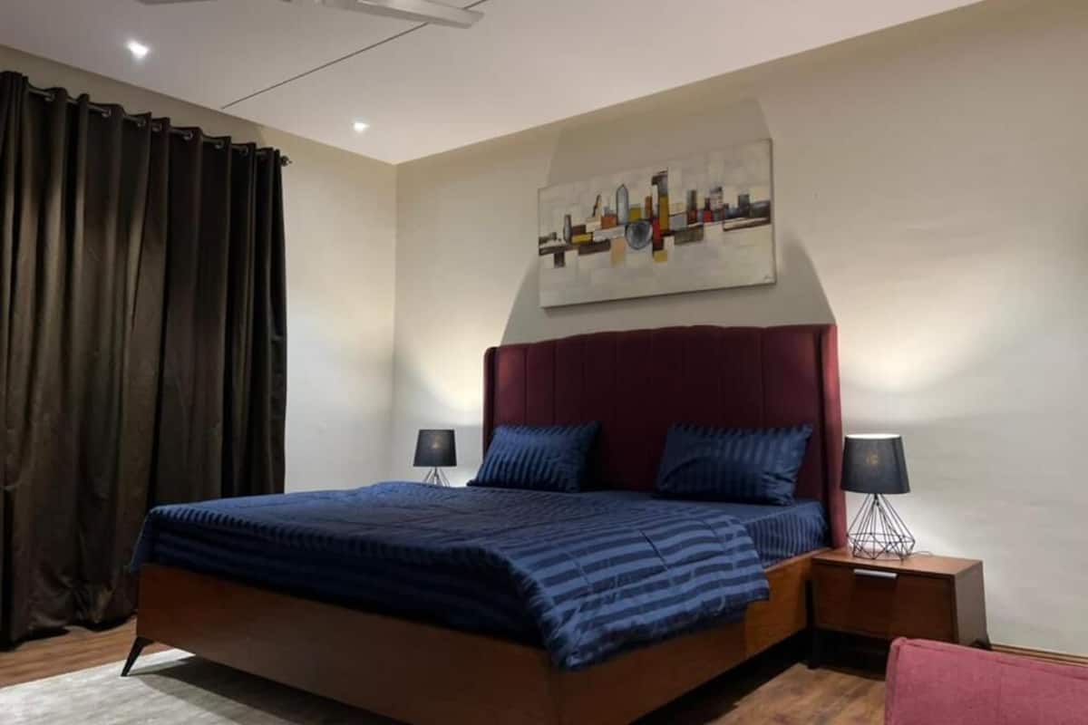 Ein Schlafzimmer mit einem großen Bett, einem Deckenventilator, einem Stadtbildgemälde an der Wand und einem Nachttisch mit Lampe.