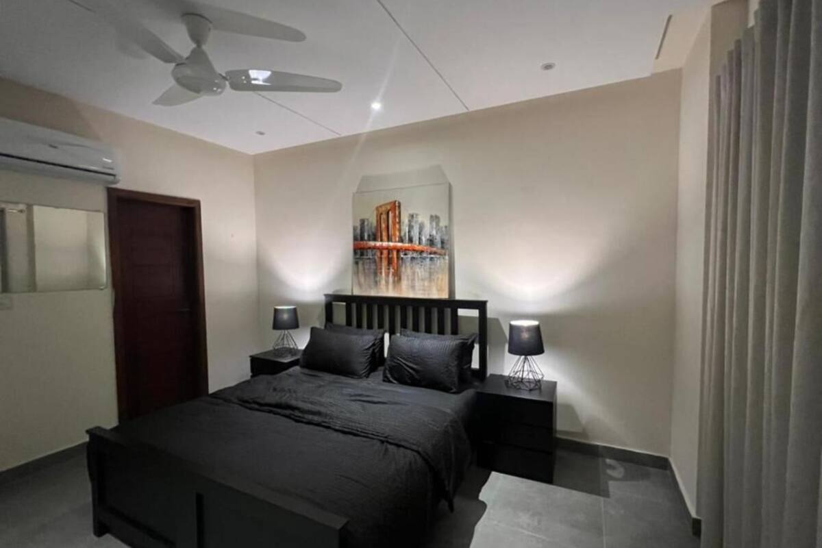 Ein Schlafzimmer mit einem Bett, einem Deckenventilator, einem Nachttisch mit Lampe und einem Bild an der Wand.