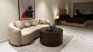 Uma sala de estar moderna com um sofá bege, uma mesa de centro redonda e um grande quadro abstrato na parede.