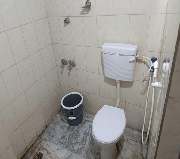 A small, tiled bathroom with a toilet, a bucket, and a shower. - Maharaja Inn (Villianur)