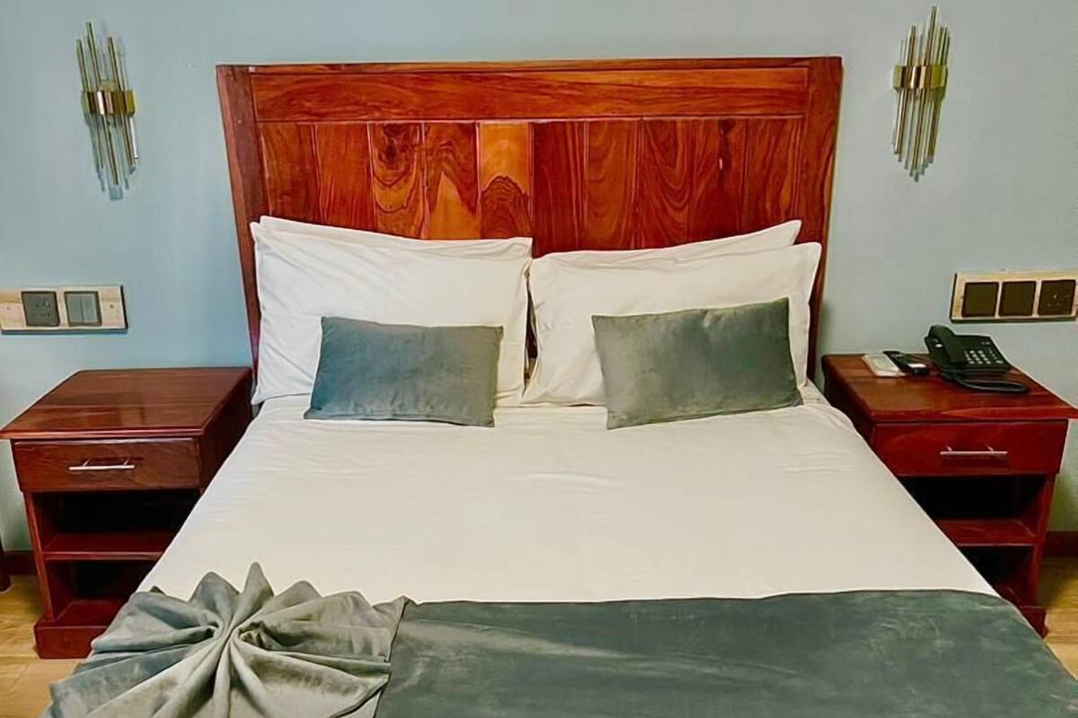 A neatly made bed with white and gray linens, a wooden headboard, and two bedside tables with lamps and a phone.