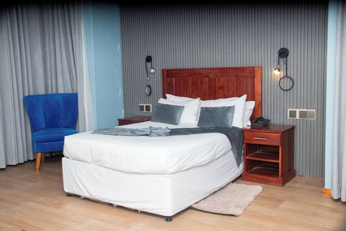 A bedroom with a bed, a nightstand, a chair, and a wall-mounted lamp.
