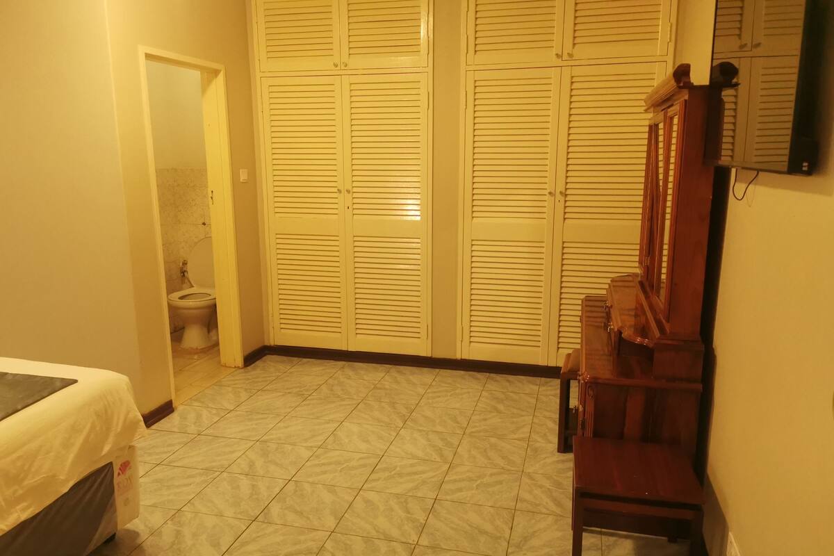 A bedroom with a bed, a wooden chair, a wardrobe, and a toilet.