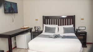 A hotel room with a bed, a desk, a coffee machine, a TV, and a small refrigerator.