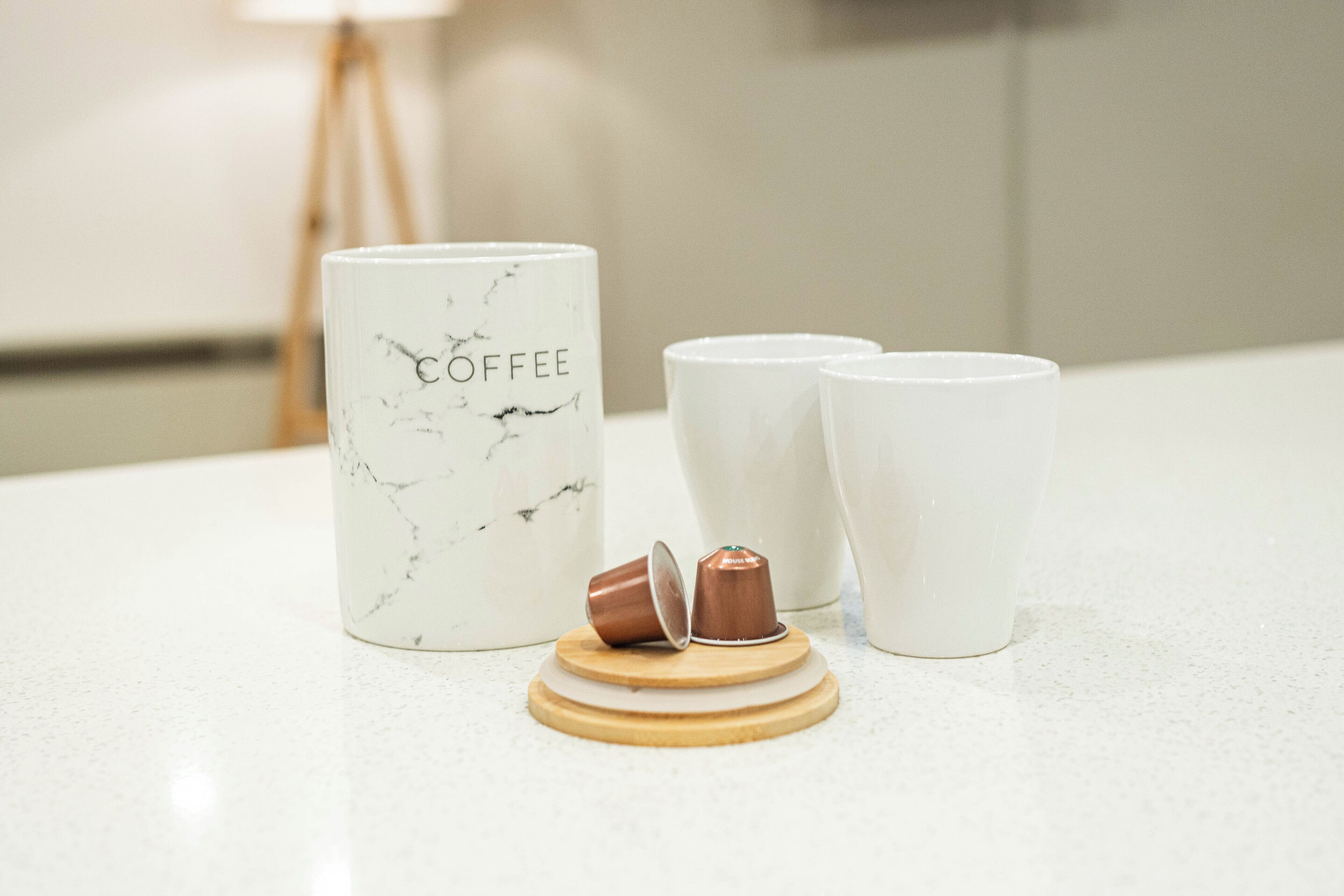 A marble-patterned coffee mug with "COFFEE" written on it, two plain white mugs, and a wooden coaster with two brown mugs on it.