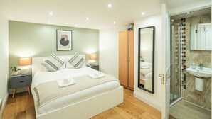 A modern bedroom with a large bed, bedside lamps, a wardrobe, and a shower area. - Stylish Camden 2-Bed Next to Camden Station (London)
