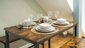 A dining table set with white plates, bowls, and glasses, with a woven placemat underneath. - Stylish Camden 2-Bed Next to Camden Station (London)