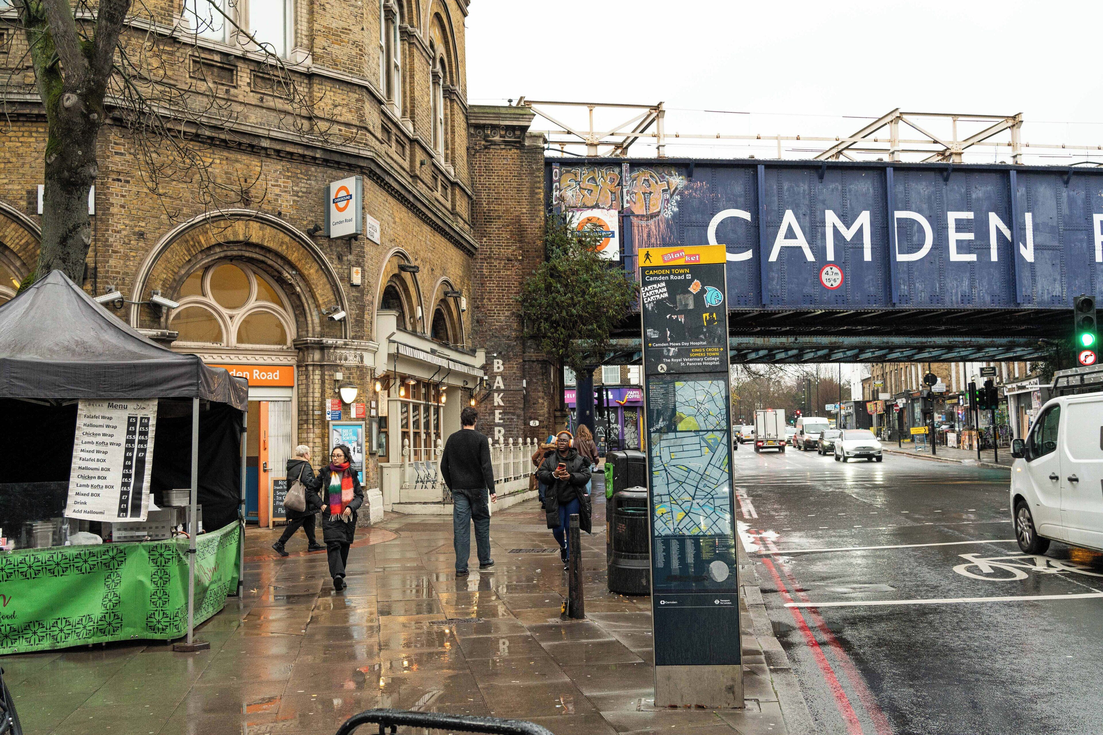 A street scene with a tram line, a green food stall, and a pedestrian crossing.
