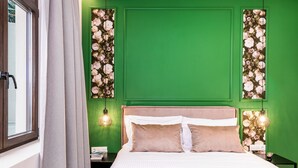 En pænt redt seng med to puder, en grøn væg med blomstret tapet og et vindue med gardiner.