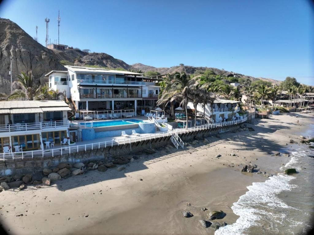 A beachfront hotel with a swimming pool, multiple balconies, and palm trees.