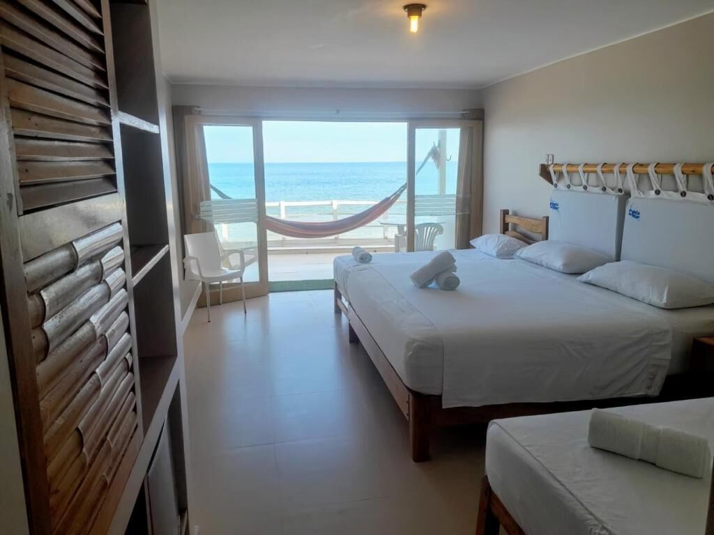 A hotel room with a large bed, a smaller bed, a hammock, and a balcony with a view of the sea.