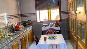 A kitchen with granite countertops, wooden cabinets, a dining table with chairs, and a window with blinds. - tayri surf house (Aourir)