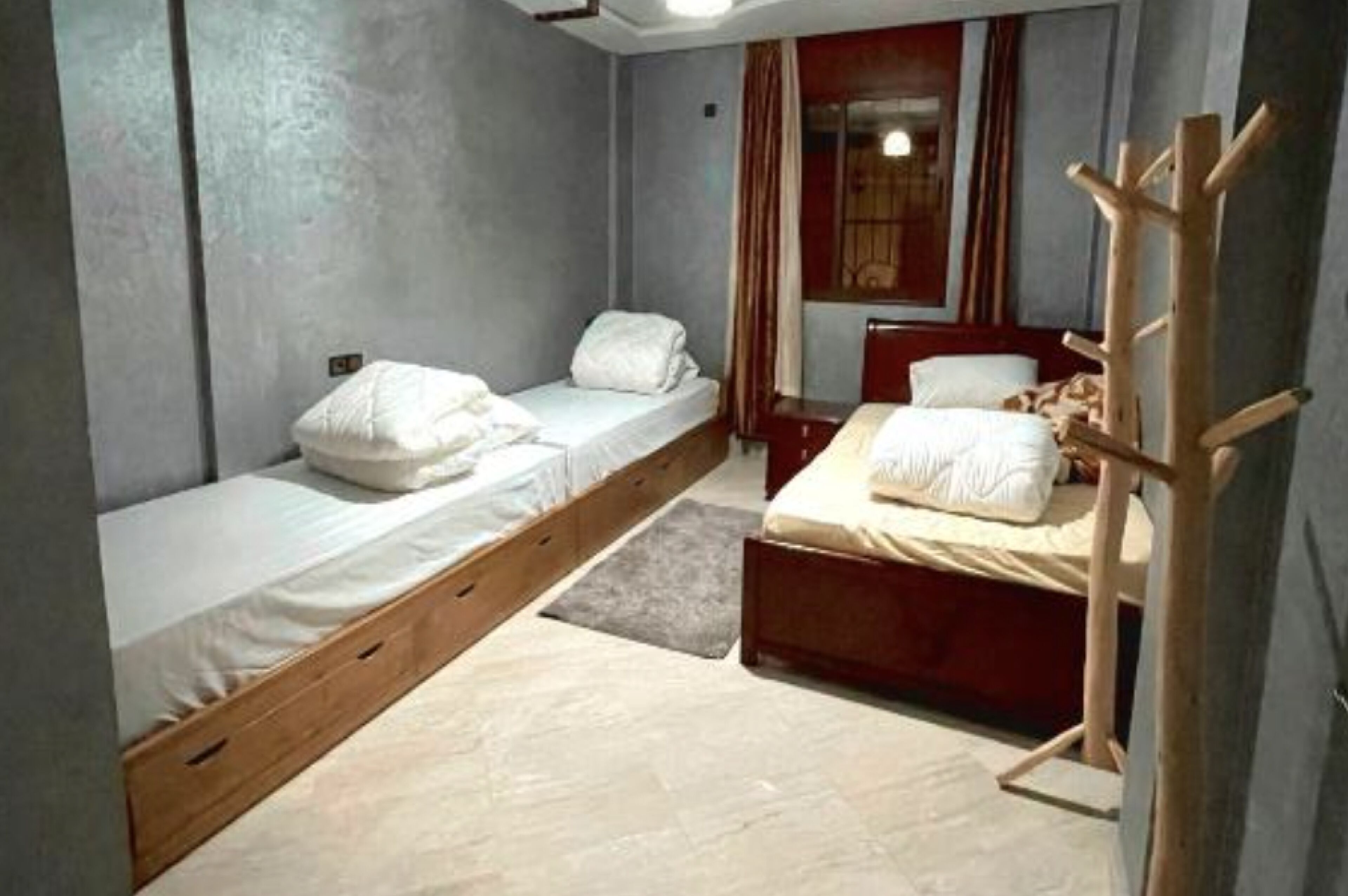A bedroom with two single beds, a wooden ladder, a window with curtains, and a red headboard.