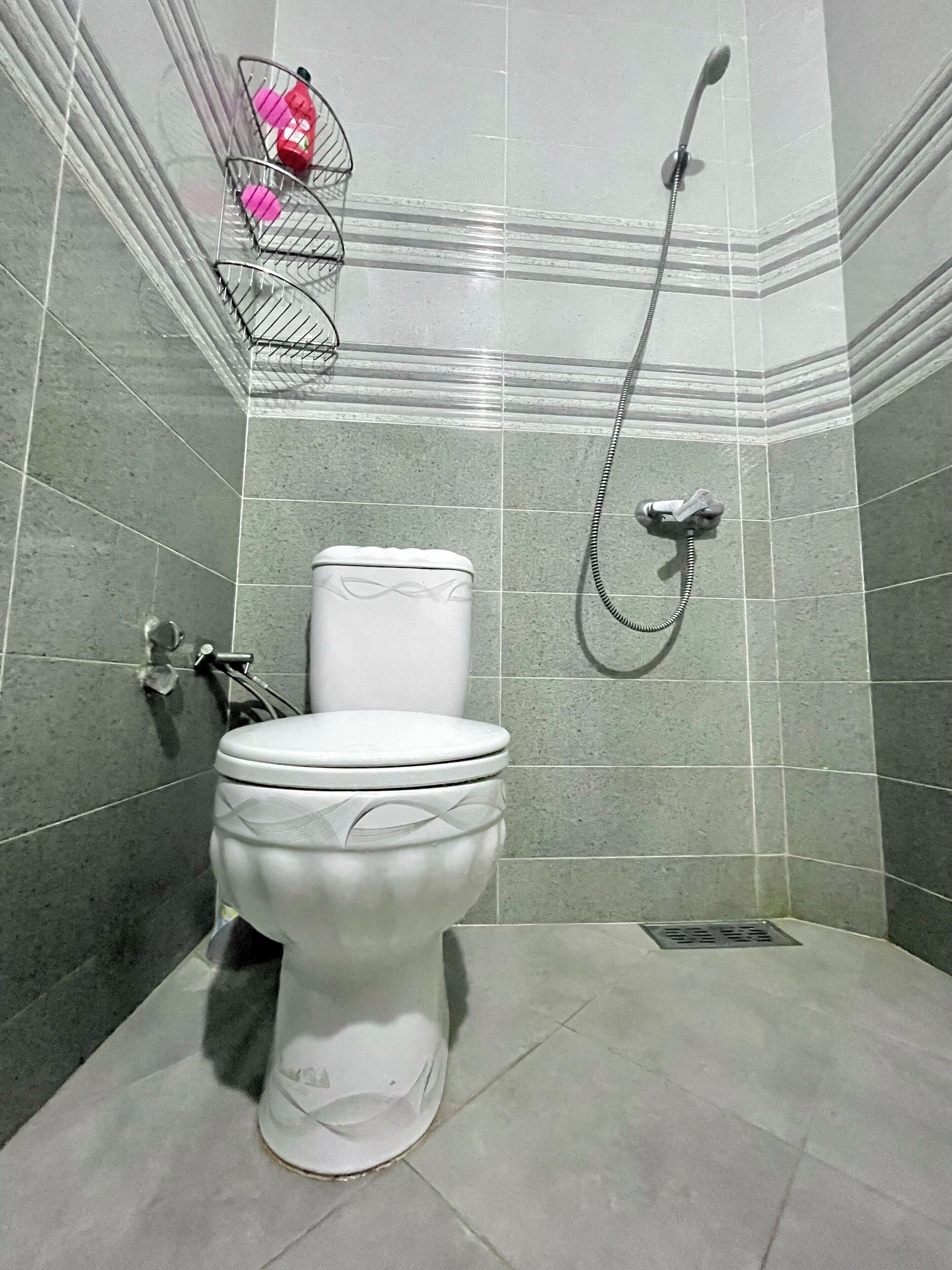 A bathroom with a toilet, a shower, and a tiled wall.