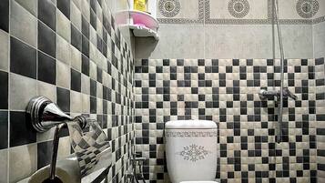 Un baño con suelo de baldosas blancas y negras en damero, un inodoro, una ducha y un dispensador de papel higiénico.