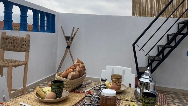 A rooftop terrace with a table set for breakfast, including bread, eggs, and bananas. - tayri surf house (Aourir)