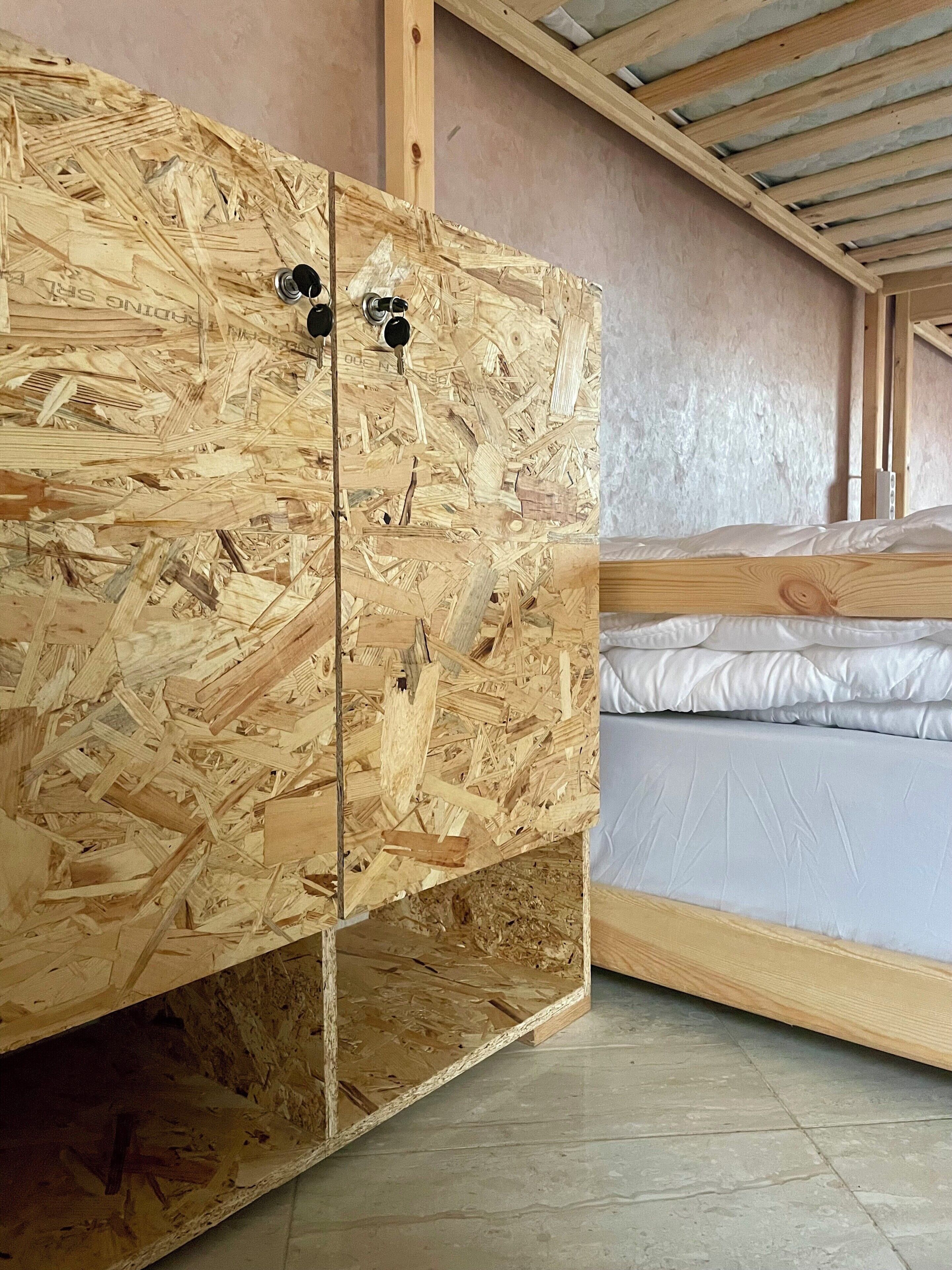 A room with a wooden bunk bed, a wooden wardrobe with two doors, and a slanted ceiling with insulation.