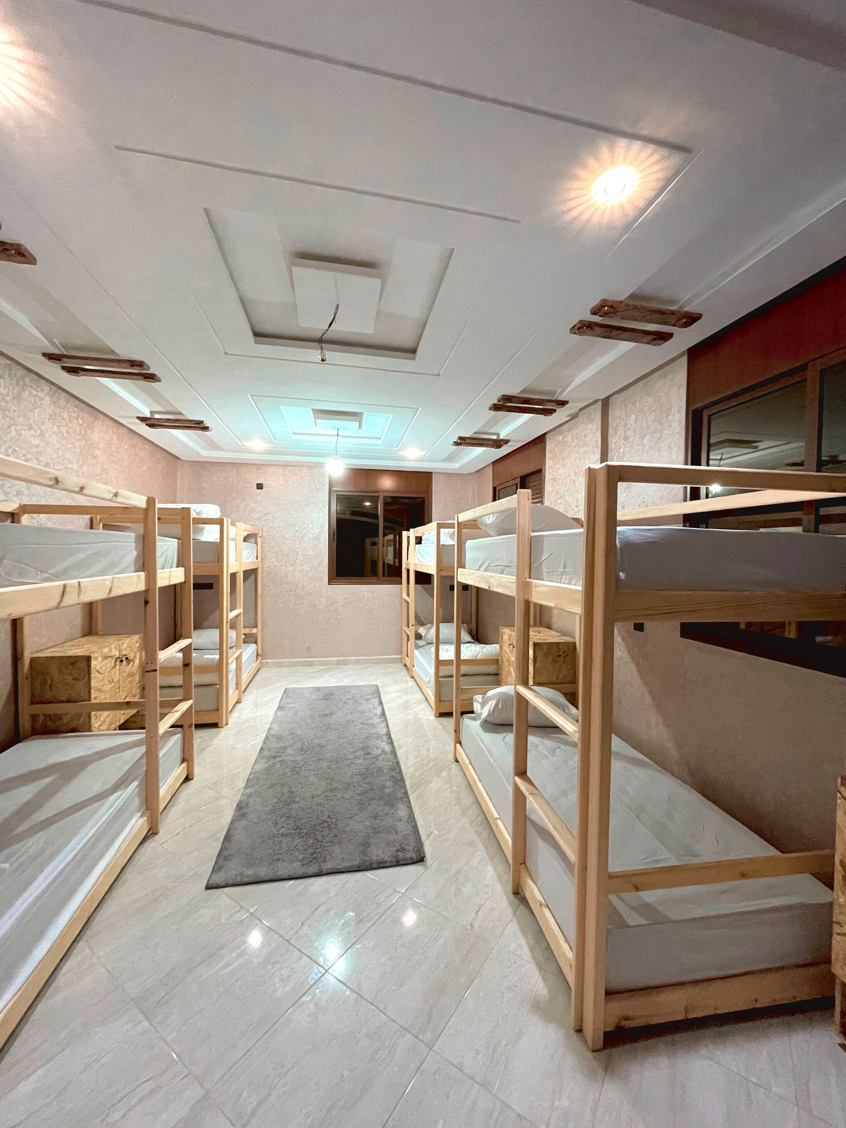 A room with bunk beds arranged in a U-shape, a grey rug, and a ceiling with recessed lighting and a skylight.