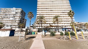 Ein Strandhotel mit mehreren Balkonen, Palmen und einem Sandweg.