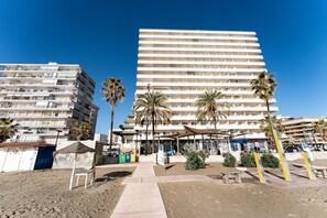 A beachfront hotel with multiple balconies, palm trees, and a sandy walkway. - Malagasuite Stella Maris Front beach (Fuengirola)