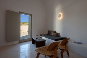 Quarto moderno com sofá, duas cadeiras de madeira, uma mesinha com garrafa e copo, e vista através de uma grande janela.