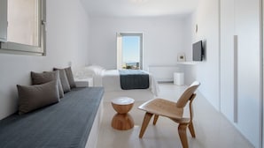A modern, minimalist bedroom with a bed, a wooden chair, a small round table, and a television on the wall. - My Rental Homes - Thera Prince with 2 pools, gym facilitiesand sea view (Fira)