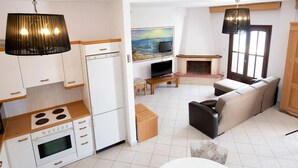 A compact living space with a kitchenette, a sofa, a television, and a fireplace. - Beach Villa by Greek Pride (Skala Fourkas)
