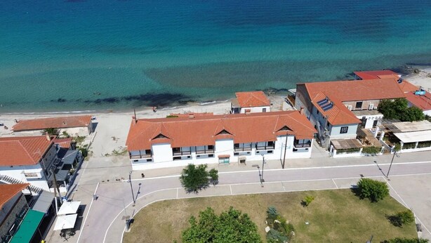 An aerial view of a coastal area with buildings, a road, and a beach. - Beach Villa by Greek Pride (Skala Fourkas)