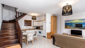 A modern kitchen with white cabinets, a dining area with a table and chairs, a wooden staircase, and a living area with a sofa and a TV. - Beach Villa by Greek Pride (Skala Fourkas)