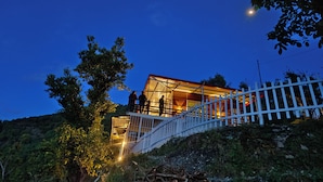 A modern house with a glass facade, a white fence, and a staircase leading up to it. -  Panoramic views of the Doon Valley and Mussoorie Hills - A Serene Hideaway. (Dhaula Giri)