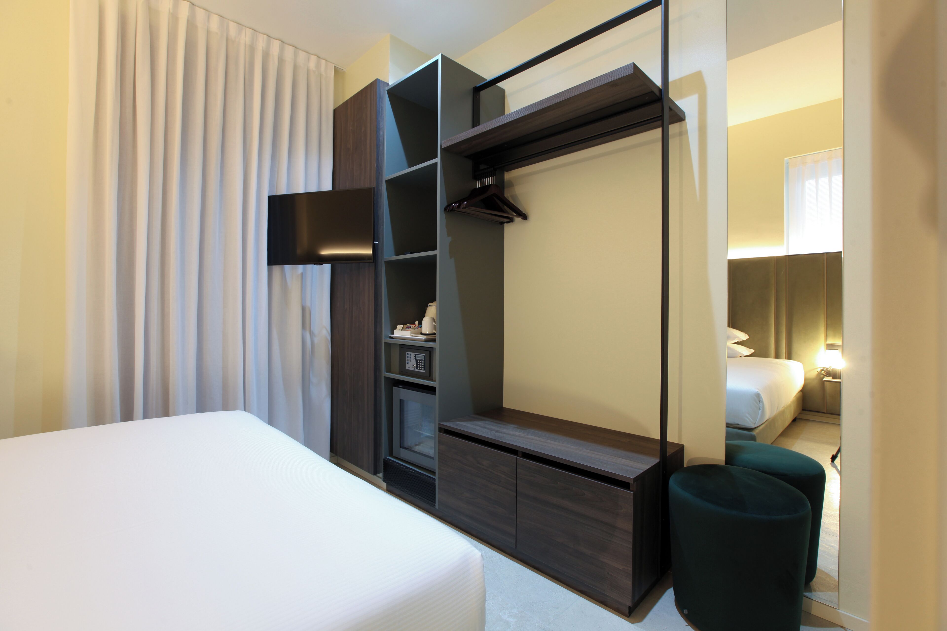 Ein modernes Hotelzimmer mit Bett, integriertem Kleiderschrank, Spiegel und Sitzecke.