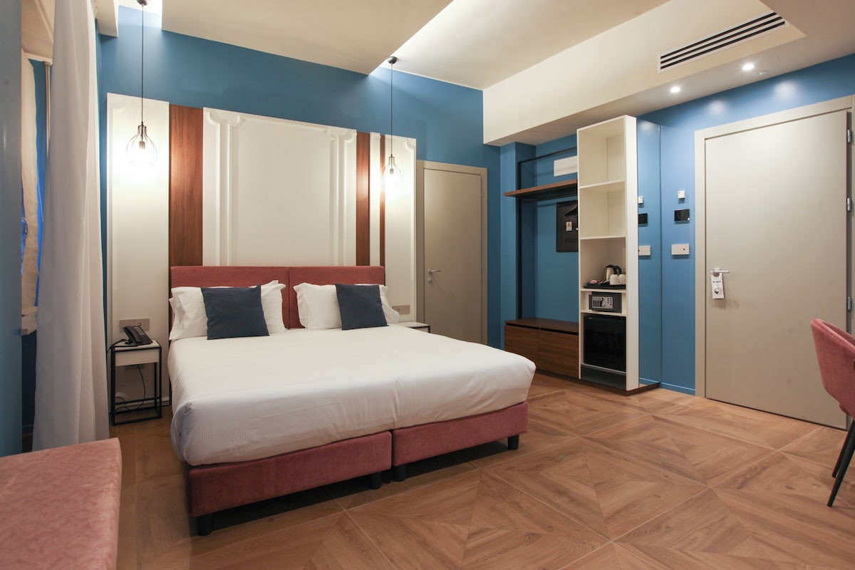 A modern bedroom with a large bed, a wardrobe, a desk, and a chair.