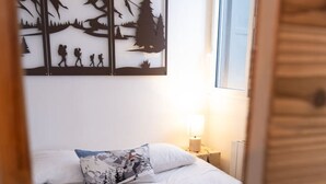 Ein Schlafzimmer mit einem Bett, weißen Leinen, einem Kopfkissen und einem an der Wand befestigten Kunstwerk, das eine Berglandschaft zeigt.