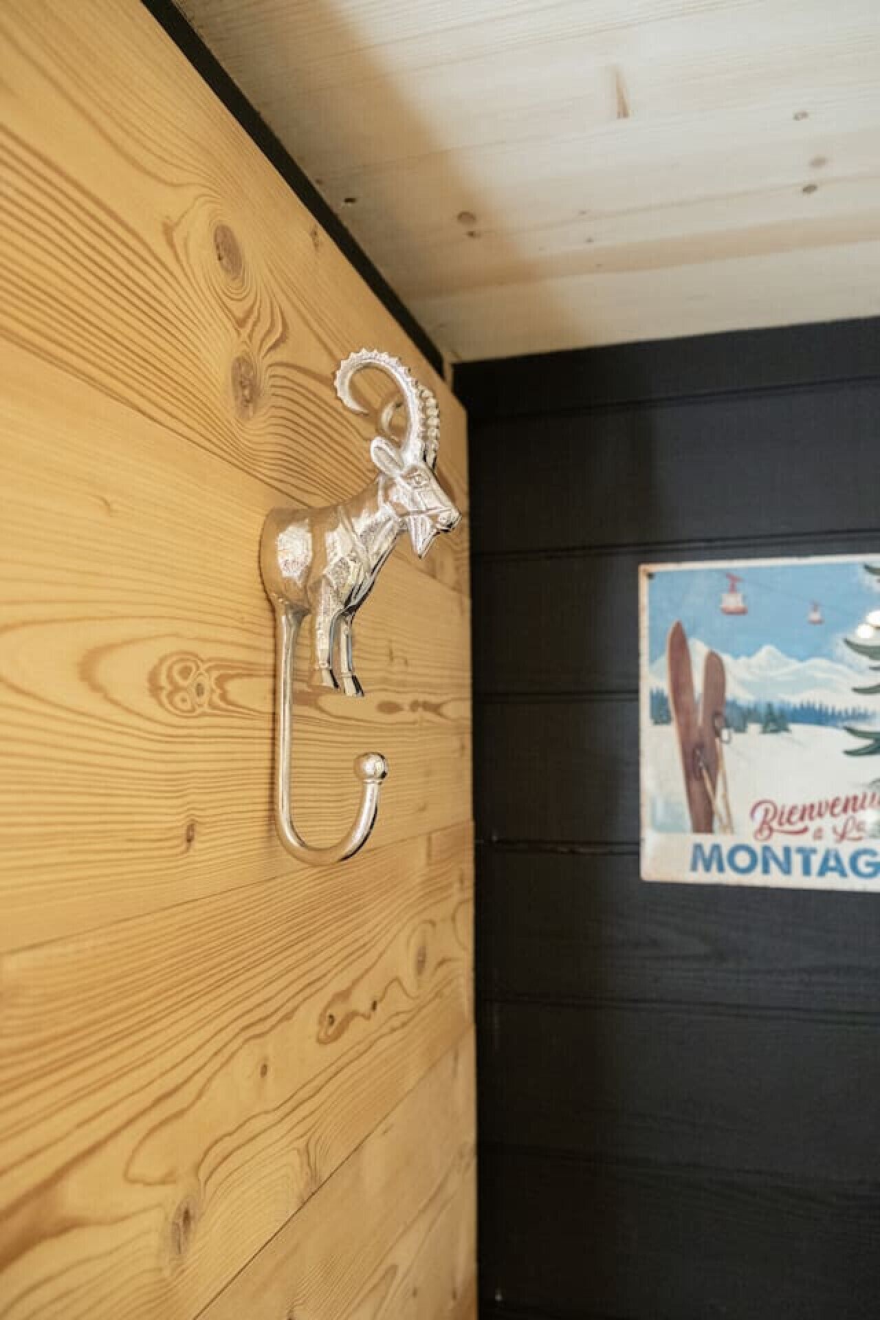 Eine Holzwand mit einem silbernen Metallhaken und einem Poster einer Skiferienregion.